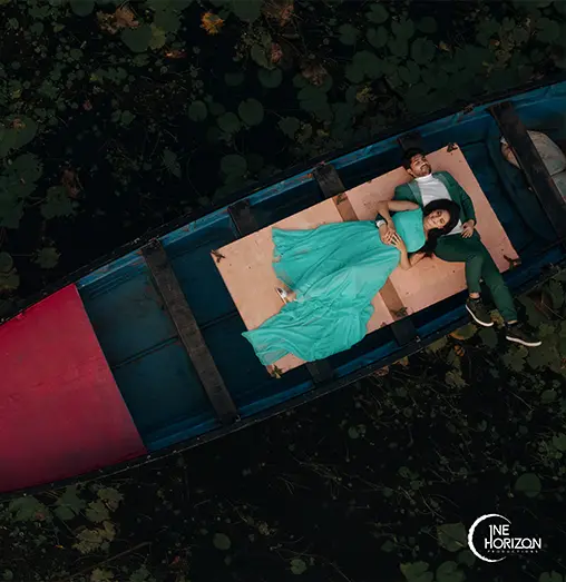 Drone shot of a couple lying on a boat surrounded by a lake filled with lotus leaves